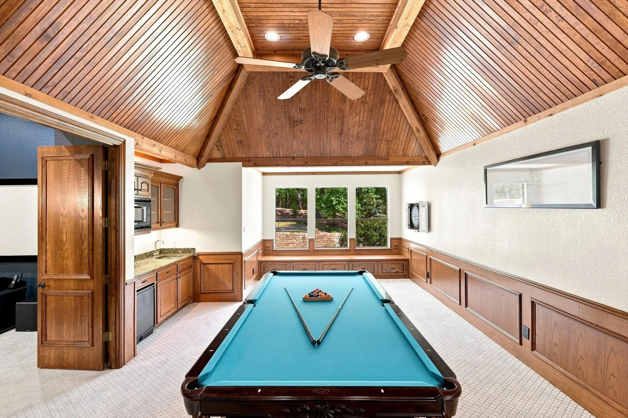 Vaulted wood-paneled ceiling with exposed beams, wood-paneled wainscoting, built-in wet bar with a microwave, and three transom windows