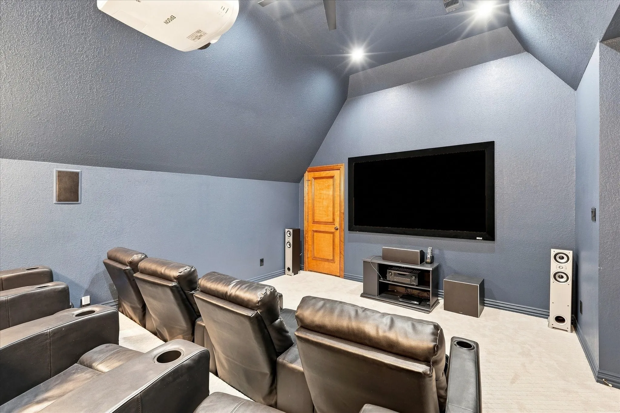 Dedicated media room featuring a large wall-mounted screen, recessed ceiling lighting, and sloped ceiling