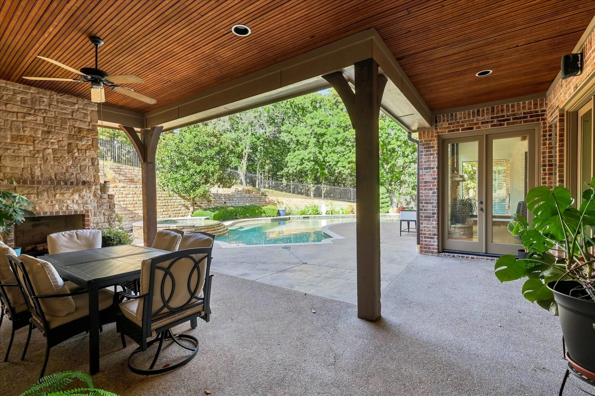 Covered patio with a wood-plank ceiling, recessed lighting, and a built-in stone fireplace
