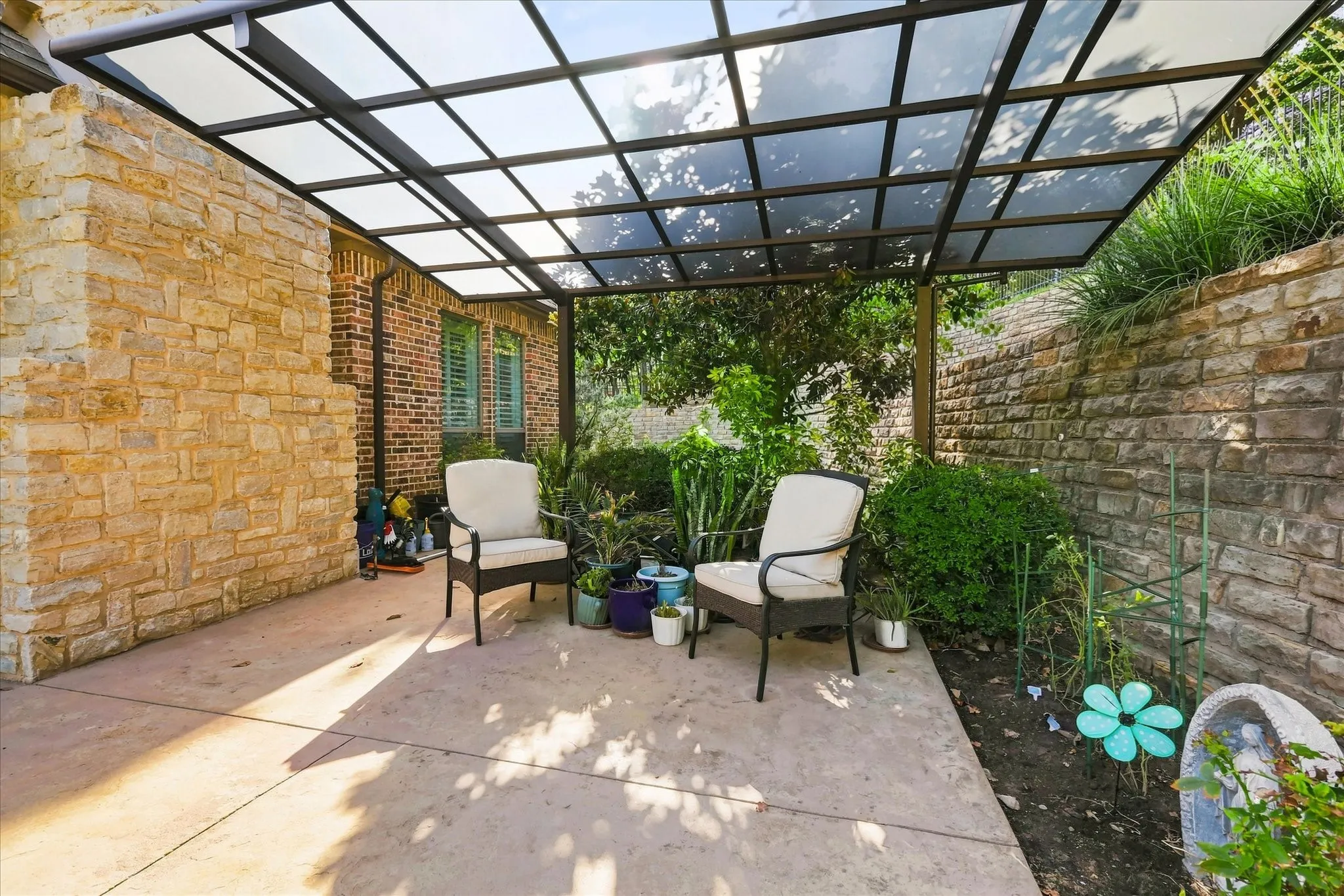 Expansive concrete patio with a modern overhead trellis, framed by a natural stone retaining wall and lush landscaping