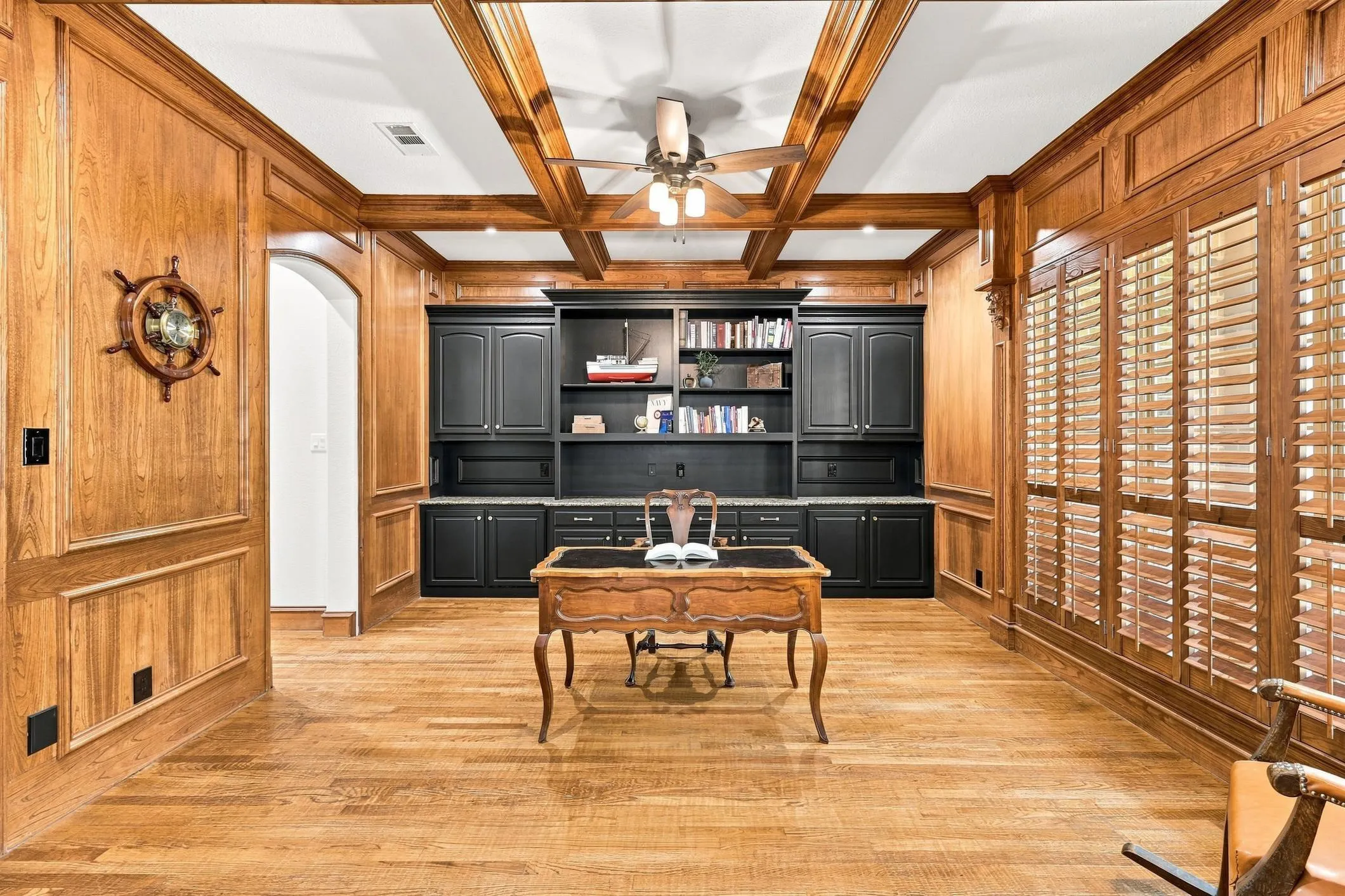 Hardwood flooring, wood paneling, built-in cabinetry, coffered ceiling, and ceiling fan