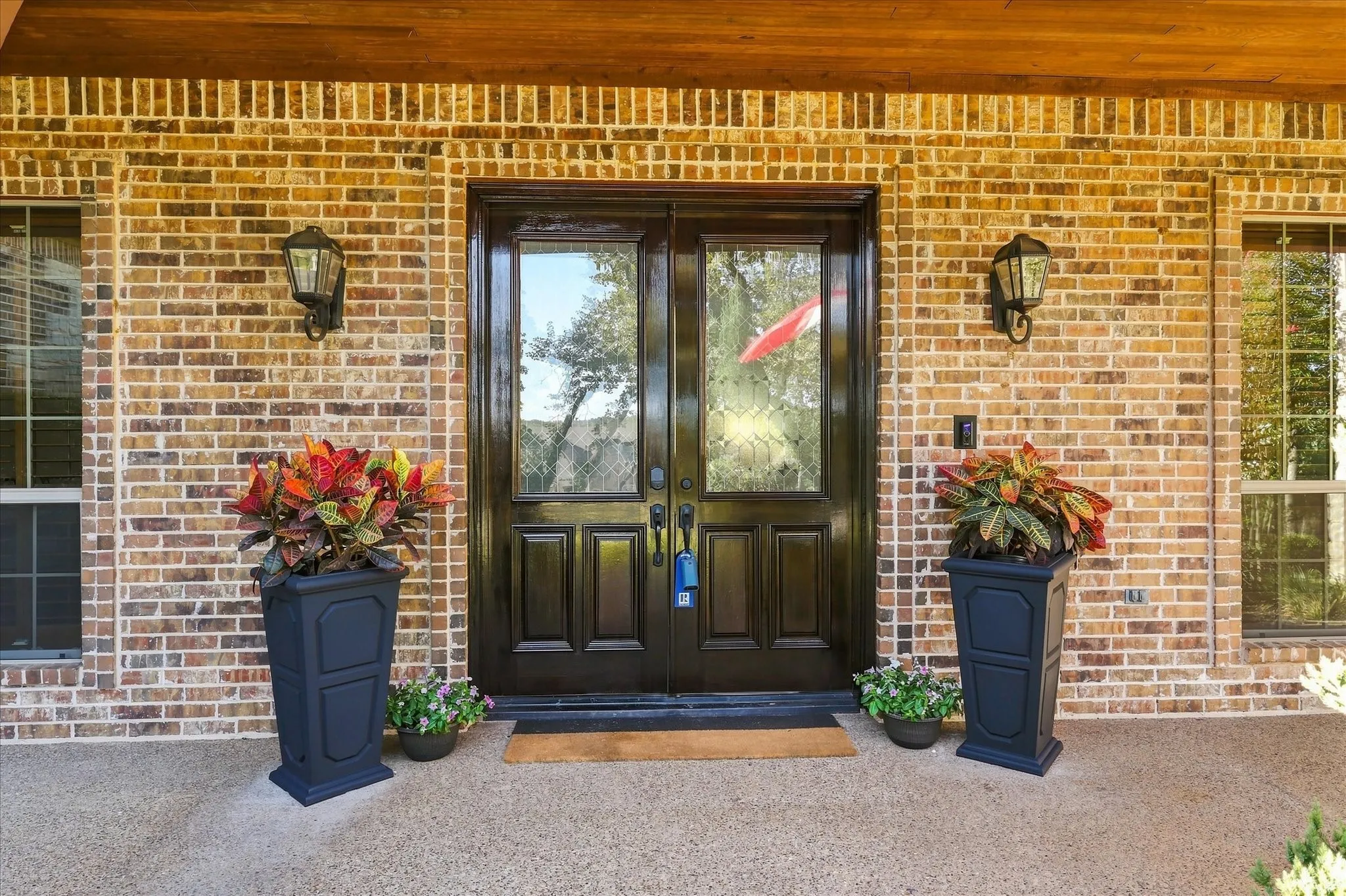 Brick exterior with a wood-paneled ceiling, featuring double entry doors with decorative glass panels, and exterior wall lanterns