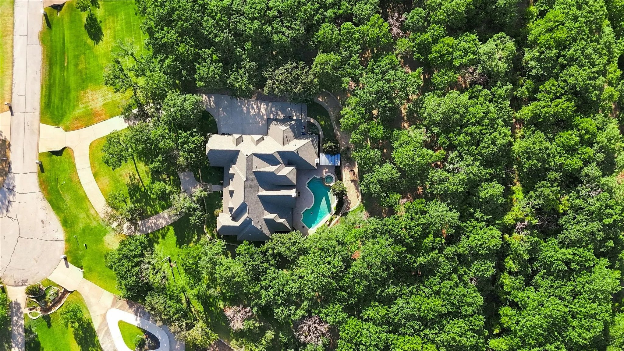 Gable roofline residence with extensive natural tree coverage, mature landscaping, and a curvilinear swimming pool