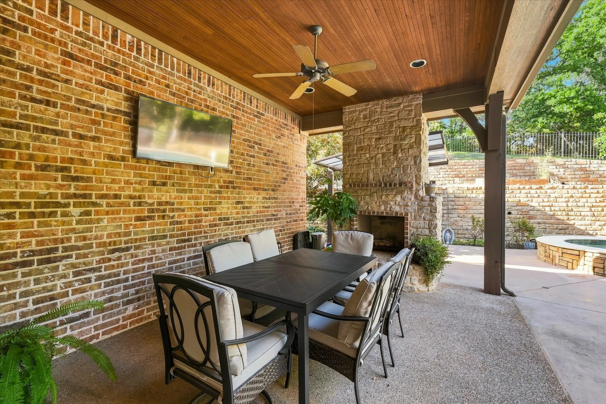 Covered patio featuring a wood-paneled ceiling, brick wall, and a stone-clad fireplace