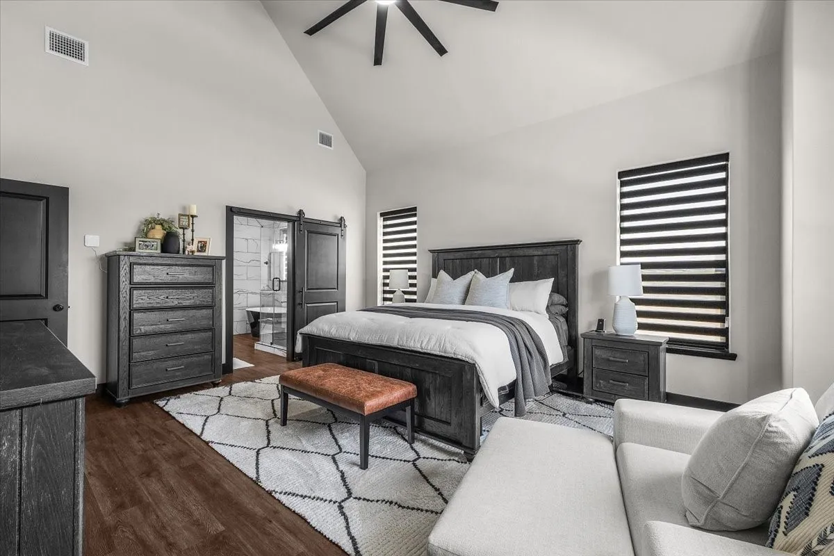 Vaulted ceiling with a ceiling fan, wood-finish flooring, barn door entry to a bathroom, and contemporary window treatments
