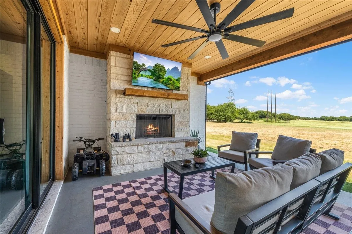 Covered patio with a wood-finish ceiling, stone fireplace, and a ceiling fan