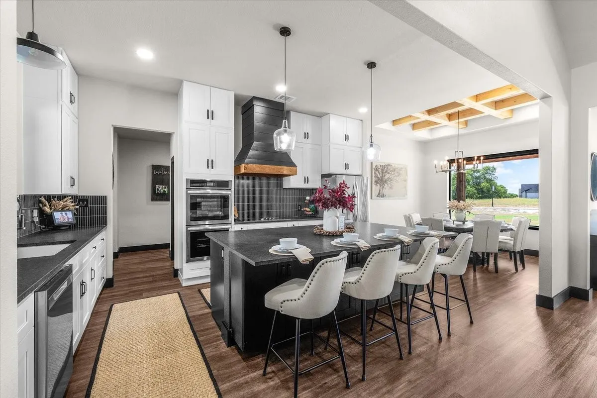 Kitchen featuring wood-finish flooring, white cabinetry, dark countertops, built-in double ovens, and an expansive island