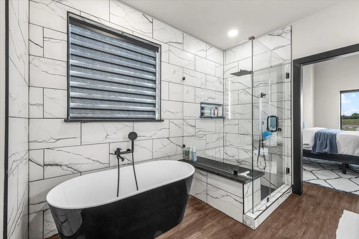Freestanding soaking tub with a floor-mounted faucet, walk-in shower with a built-in bench, marble-finish tile walls, recessed lighting, and wood-finish flooring