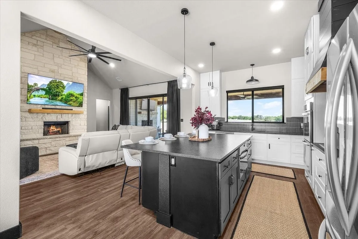 Open-concept living space featuring wood-finish flooring, a stone-clad fireplace, and a vaulted ceiling with a fan