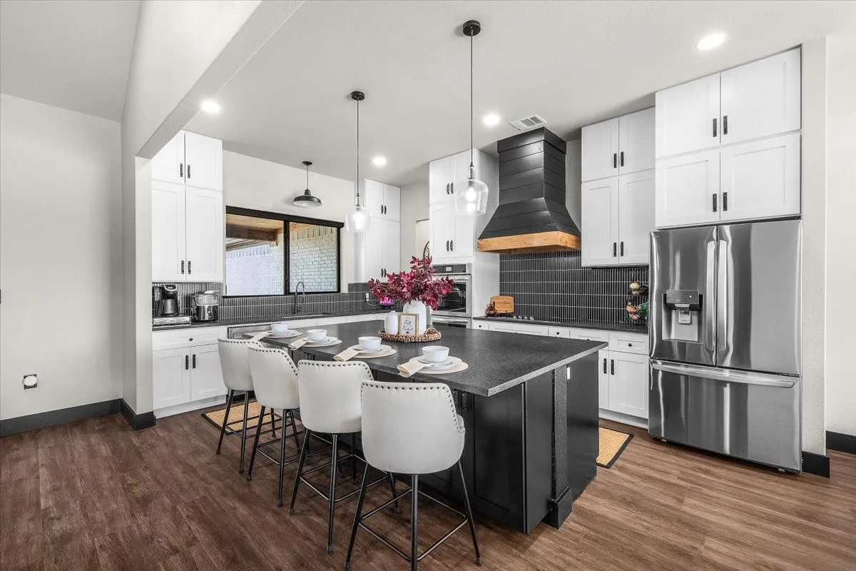 Kitchen featuring white upper and lower cabinetry, dark wood-finish flooring, a central island with countertop seating, stainless steel appliances, and a dark tile backsplash