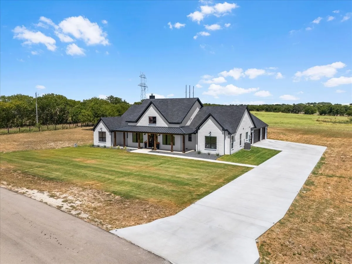 Modern farmhouse exterior with white brick facade, dark shingle roof, and a covered porch with wood columns