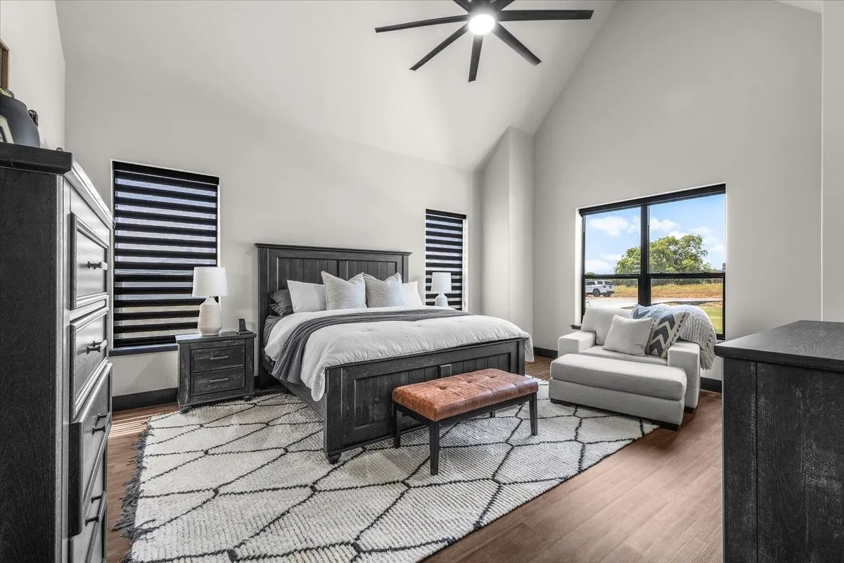 Vaulted ceiling with a ceiling fan, wood-finish flooring, and large windows with black frames