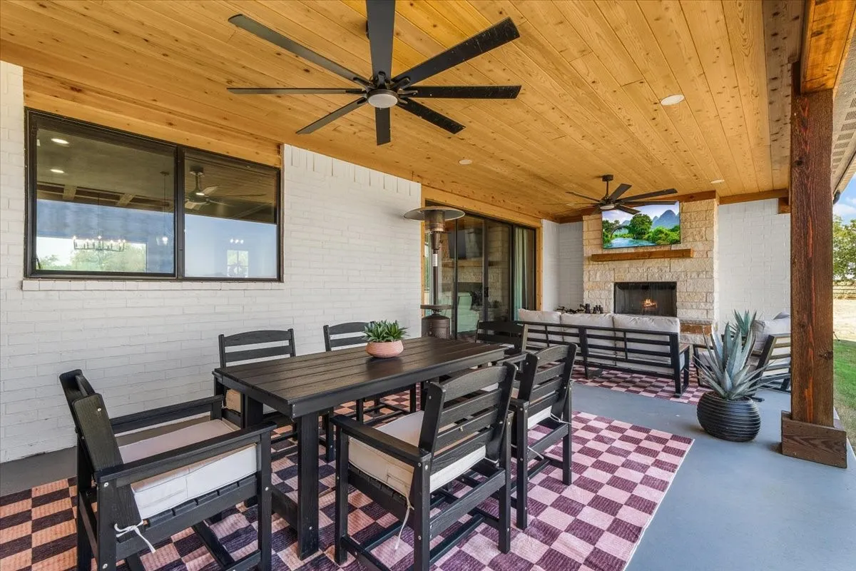 Covered patio featuring a wood-plank ceiling, two ceiling fans, and a stone-clad fireplace
