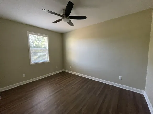 Wood-finish flooring, neutral wall tones, window with horizontal blinds, and a ceiling fan with integrated lighting