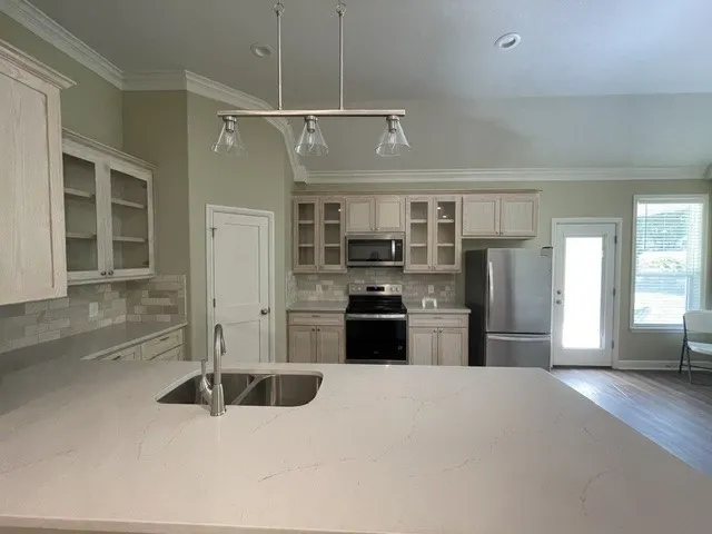 Kitchen featuring light-toned cabinetry, quartz countertops, stainless steel appliances, and a tile backsplash