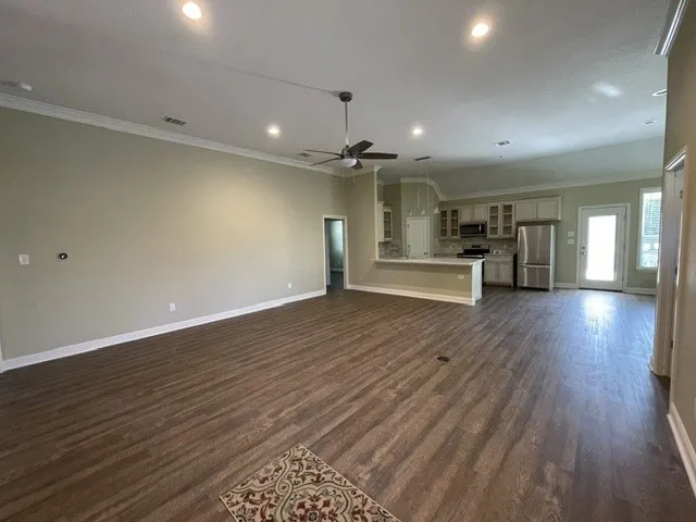 Open-concept living space featuring wood-finish flooring, recessed lighting, a ceiling fan, and crown molding