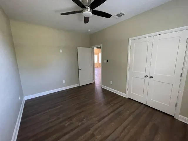 Wood-finish flooring, neutral wall tones, ceiling fan with light fixture, white interior doors, and white trim