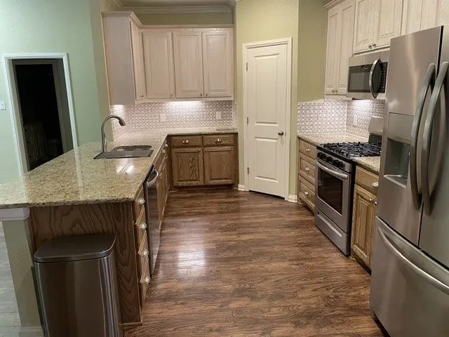 U-shaped kitchen featuring wood-finish flooring, light-toned upper cabinetry, stainless steel appliances, granite-style countertops, and a decorative tile backsplash