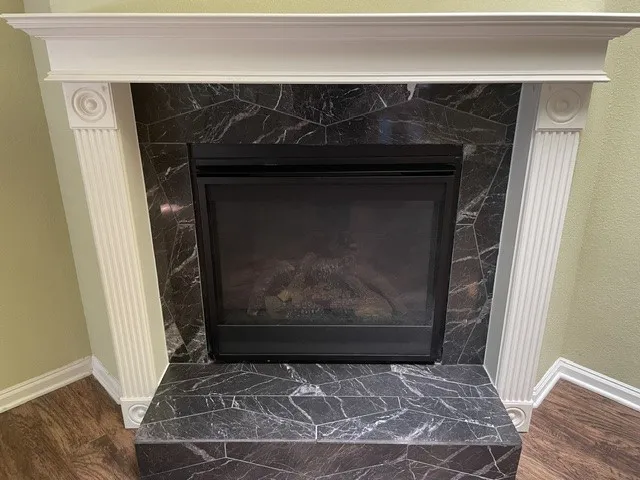 Corner fireplace featuring a black-marbled surround, decorative white mantel, and black firebox
