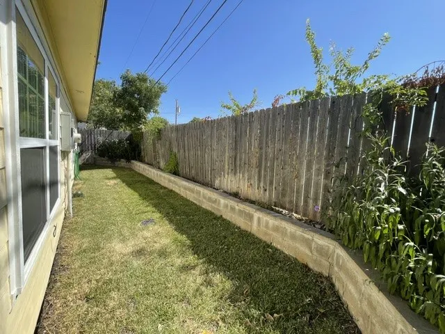 Side yard featuring a wood fence, concrete retaining wall, and established plantings