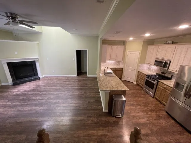  wood-finish flooring, fireplace with stone surround, kitchen island with sink, stainless steel appliances