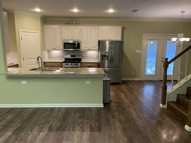 Kitchen featuring stainless steel appliances, light-toned cabinetry, granite countertops, and a tiled backsplash