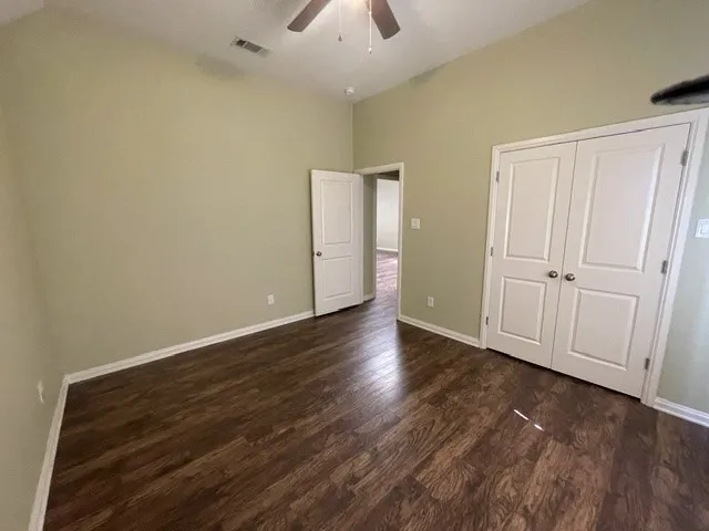 Spacious room featuring wood-finish flooring, light green walls, a vaulted ceiling, and a ceiling fan