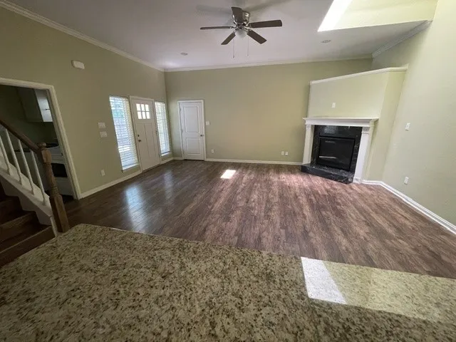 Spacious living area featuring high ceilings, wood-finish flooring, a ceiling fan, and a fireplace with a stone surround