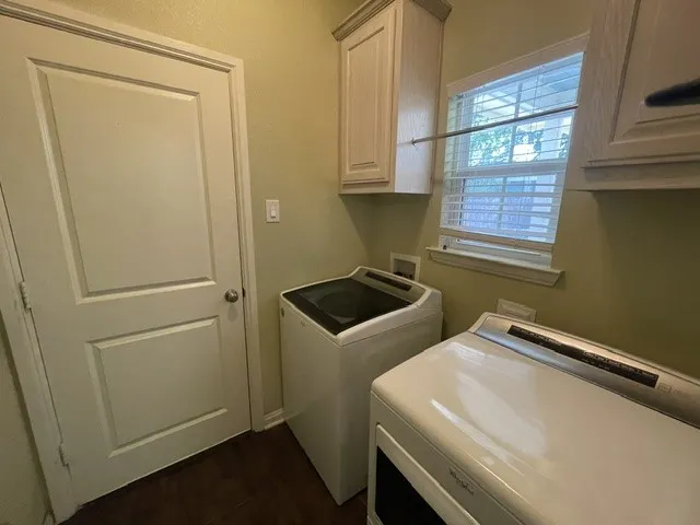 Upper cabinetry, window with blinds, and rich wood-finish flooring