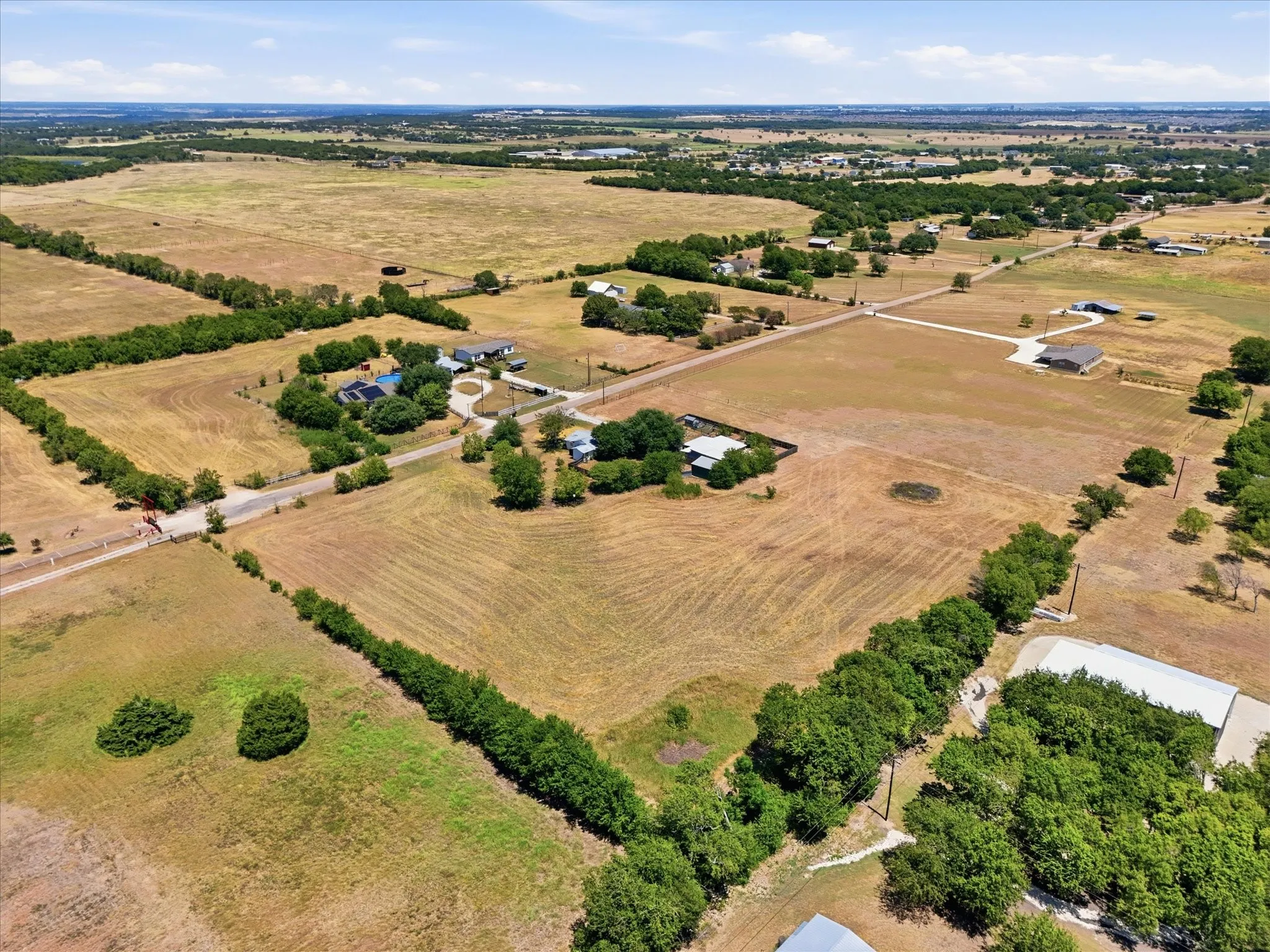 Expansive acreage with established tree lines, a paved road, and visible structures, featuring clear land