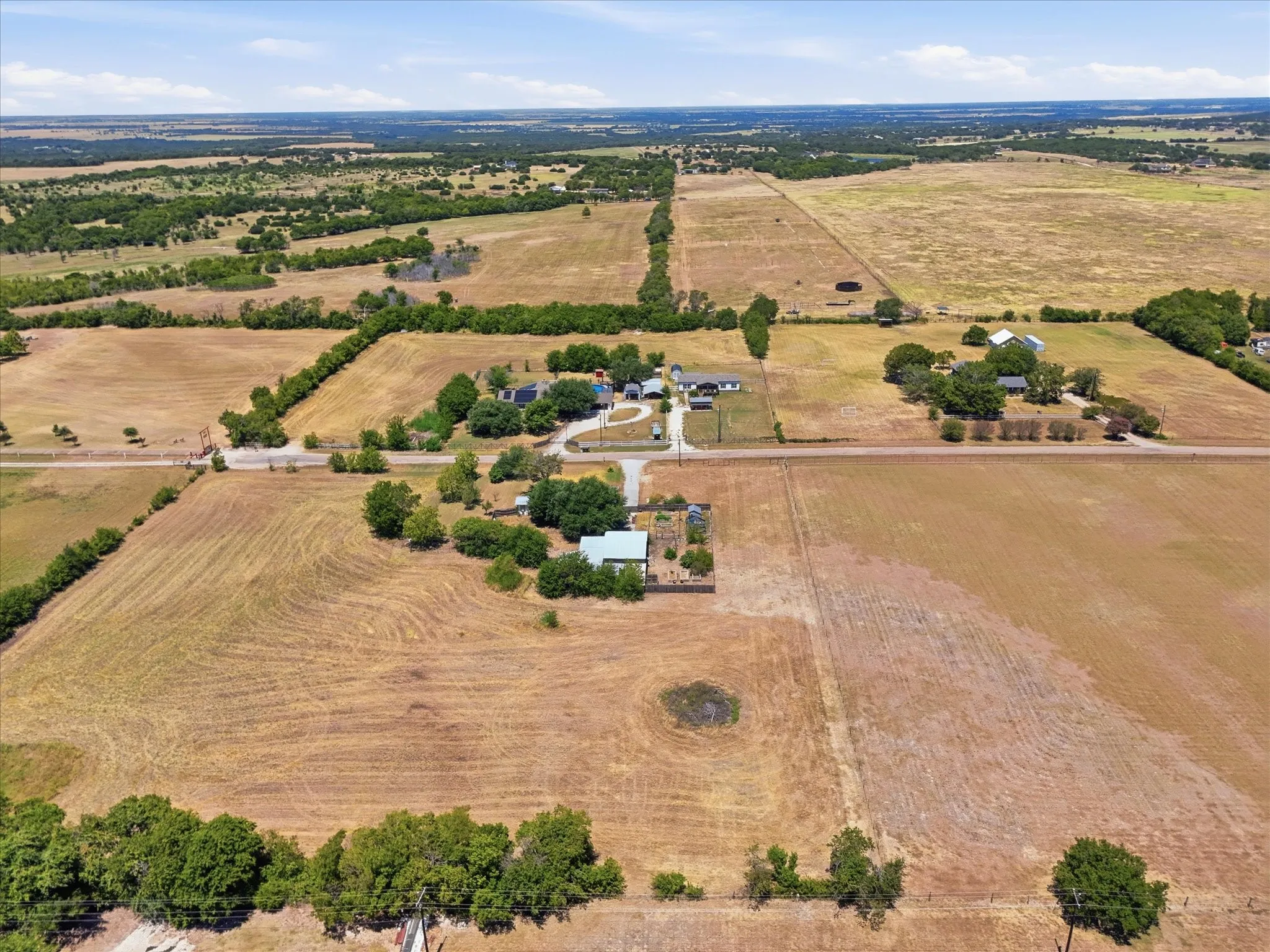 Expansive agricultural land with a distant rural landscape, featuring multiple buildings and scattered mature trees