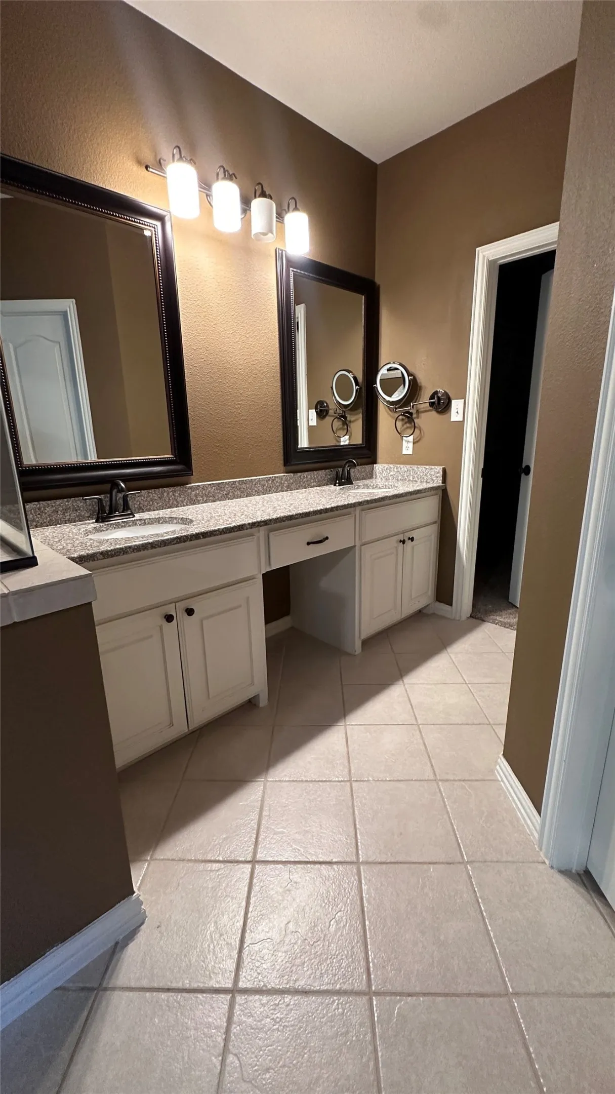 Dual vanity with light-toned granite countertops, white cabinetry, and framed mirrors