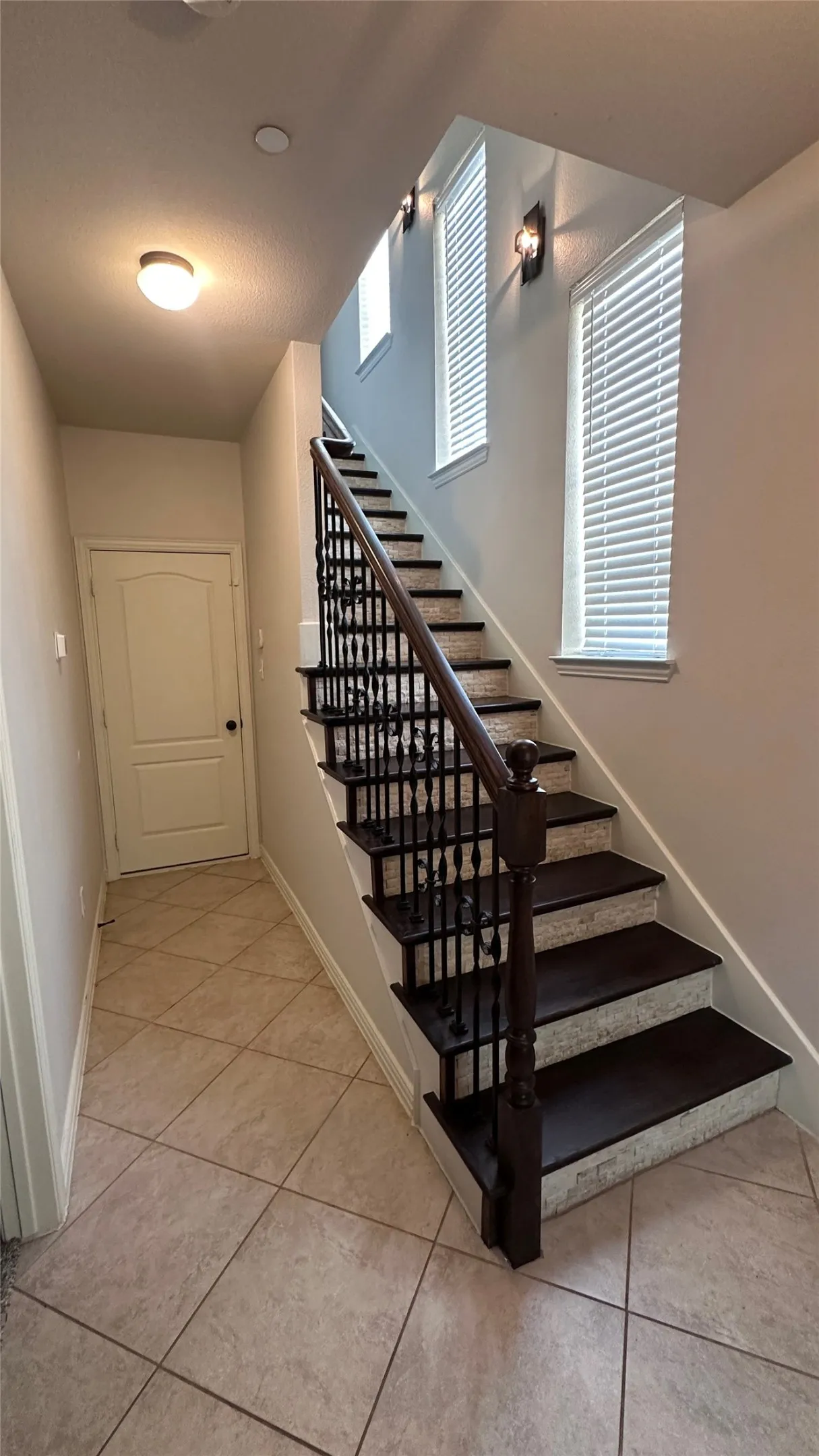 Tiled flooring entryway featuring a staircase with dark wood-finish treads, decorative metal balusters, and a wood newel post