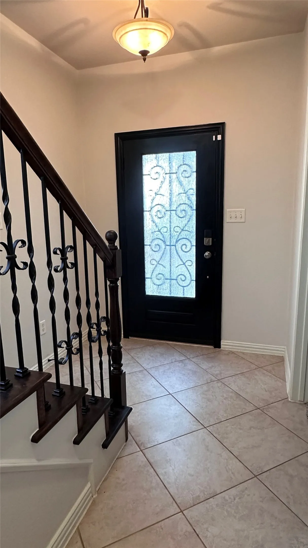 Entryway featuring a decorative glass paneled door, tiled flooring, wood-finish staircase with wrought iron balusters, and a semi-flush ceiling fixture