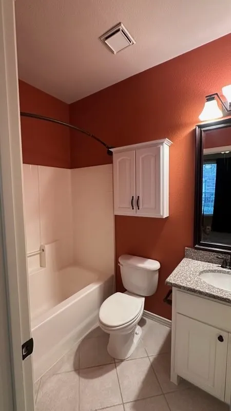 Bathroom featuring a white vanity with a light-toned countertop, a white toilet, a built-in wall cabinet, and a shower-tub combination with a curved shower rod