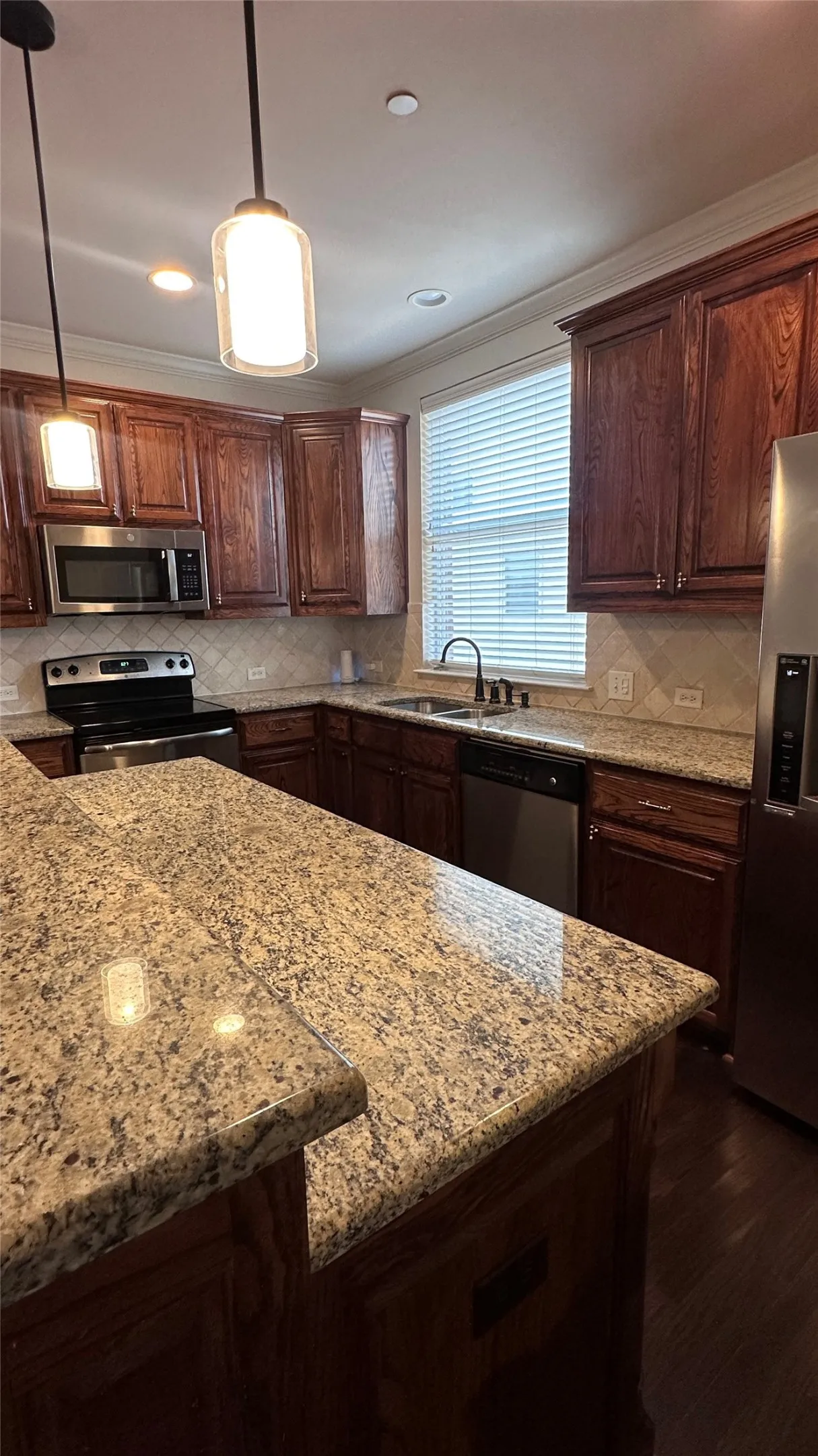 Kitchen featuring wood cabinetry, stainless steel appliances, speckled stone countertops, and a tile backsplash