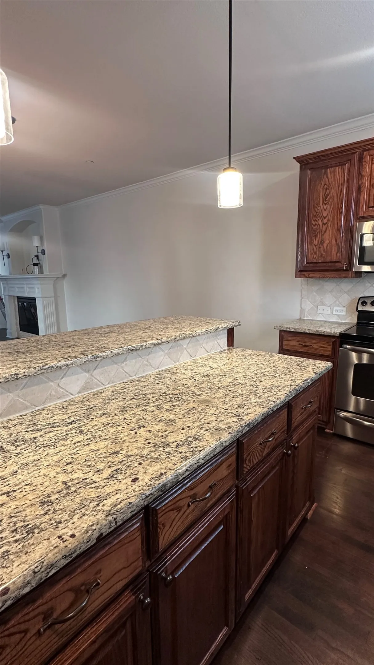 Granite countertops, dark wood cabinetry, tile backsplash, stainless steel appliances, and crown molding