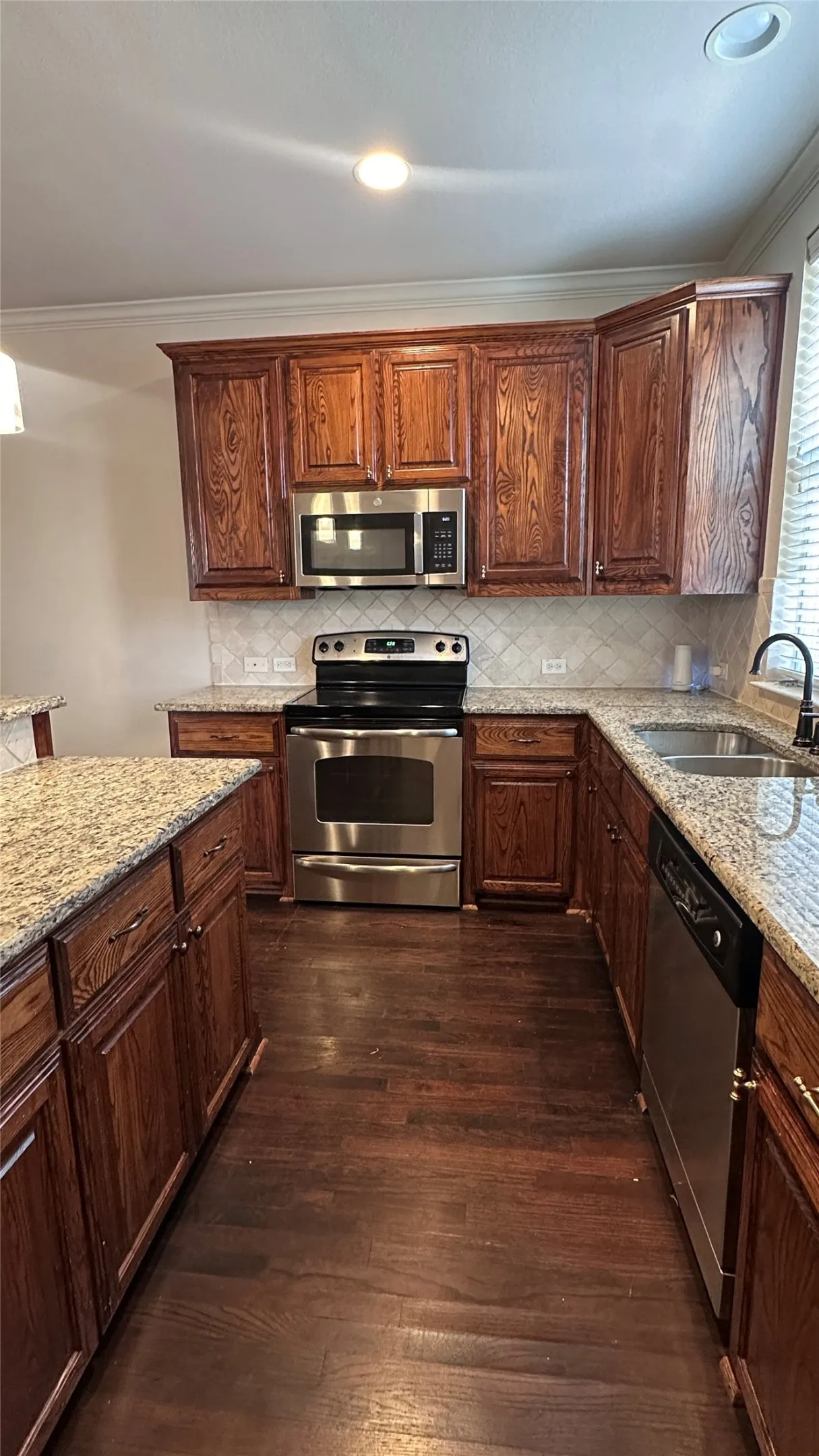Kitchen featuring granite countertops, wood cabinetry, stainless steel appliances, a tile backsplash, and wood-finish flooring