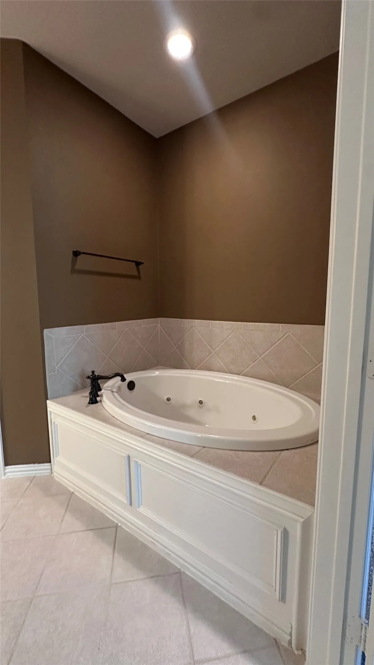 Corner jetted tub with white paneling and a tiled surround, featuring a dark bronze faucet