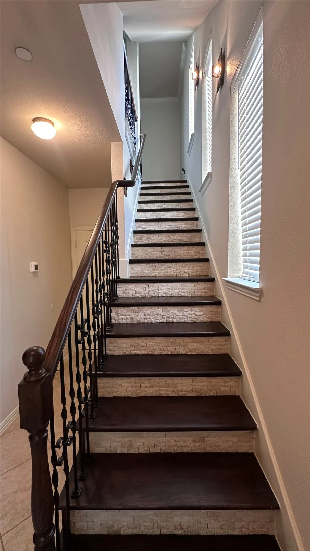 Staircase featuring dark wood treads, textured risers, and wrought iron balusters with a wood handrail
