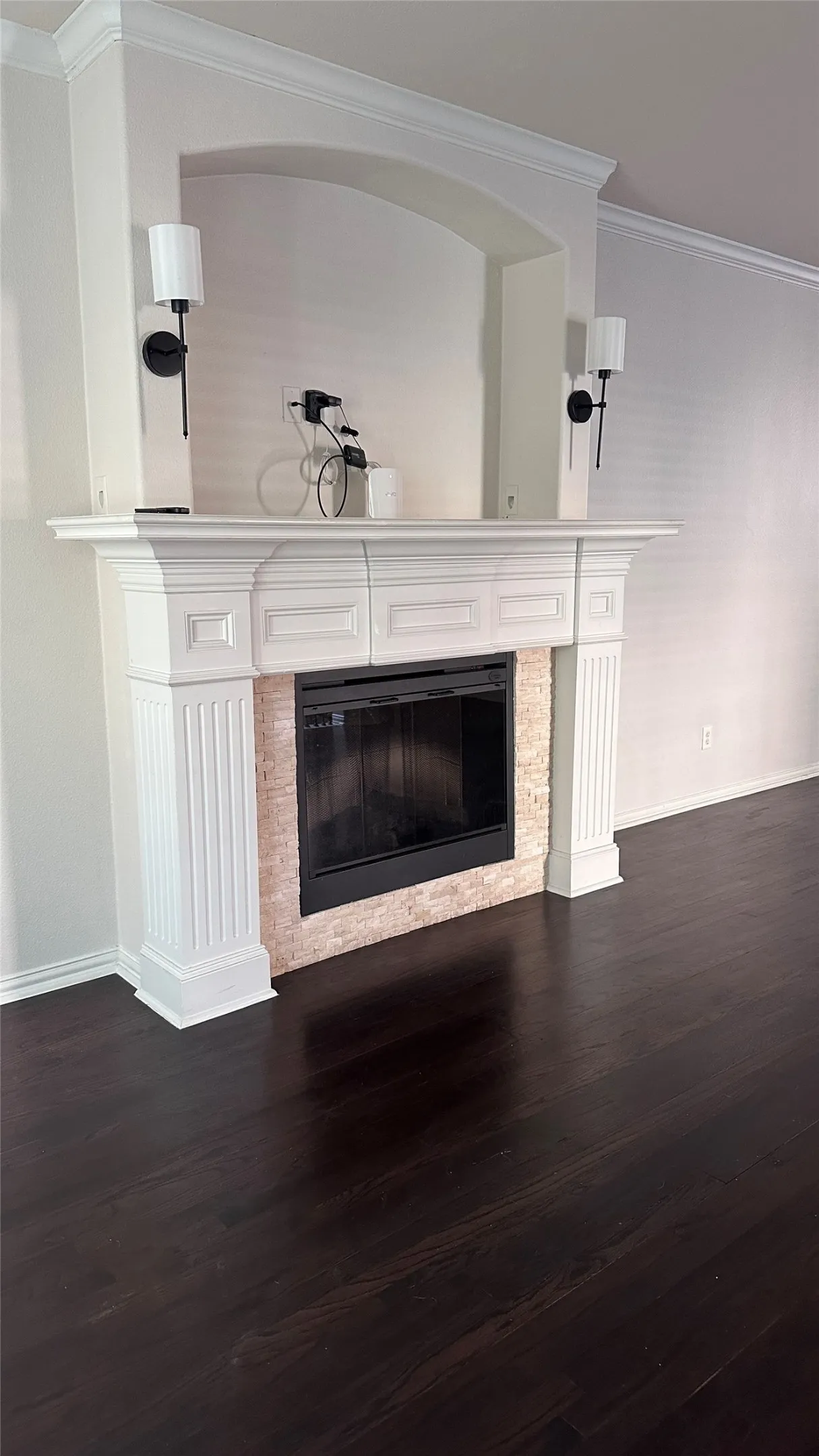 Fireplace with decorative mantle, stone tile surround, and arched niche, complemented by dark wood-finish flooring and wall-mounted sconces