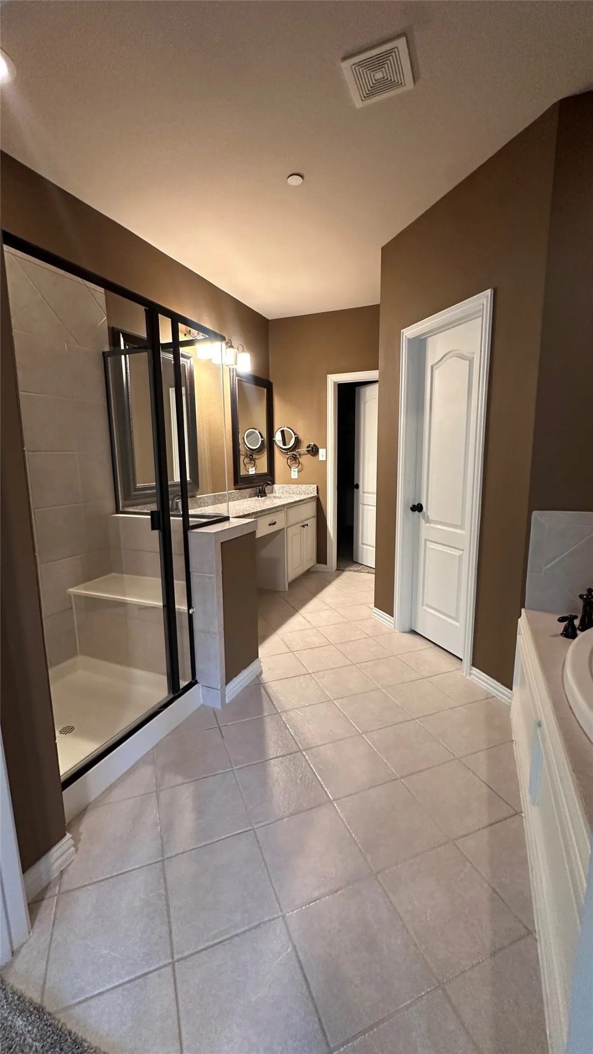 Spacious bathroom featuring a large shower with built-in bench, dual vanity with undermount sinks, and tile flooring