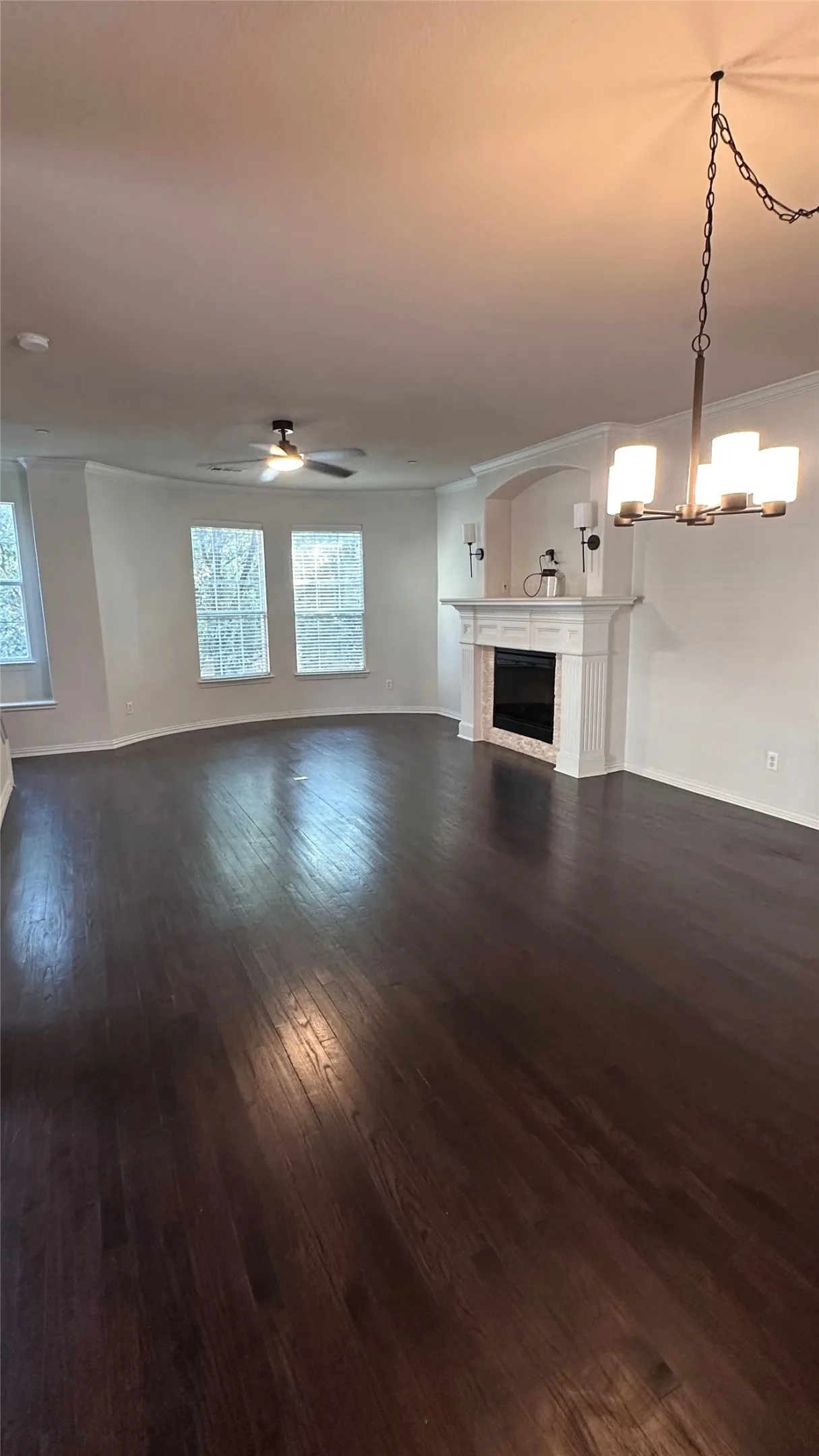 Dark wood-finish flooring, white fireplace with a decorative mantel, arched alcove, contemporary chandelier, and ceiling fan