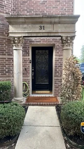 Brick exterior with stone columns, a decorative transom, and a paneled entry door with intricate wrought iron detailing
