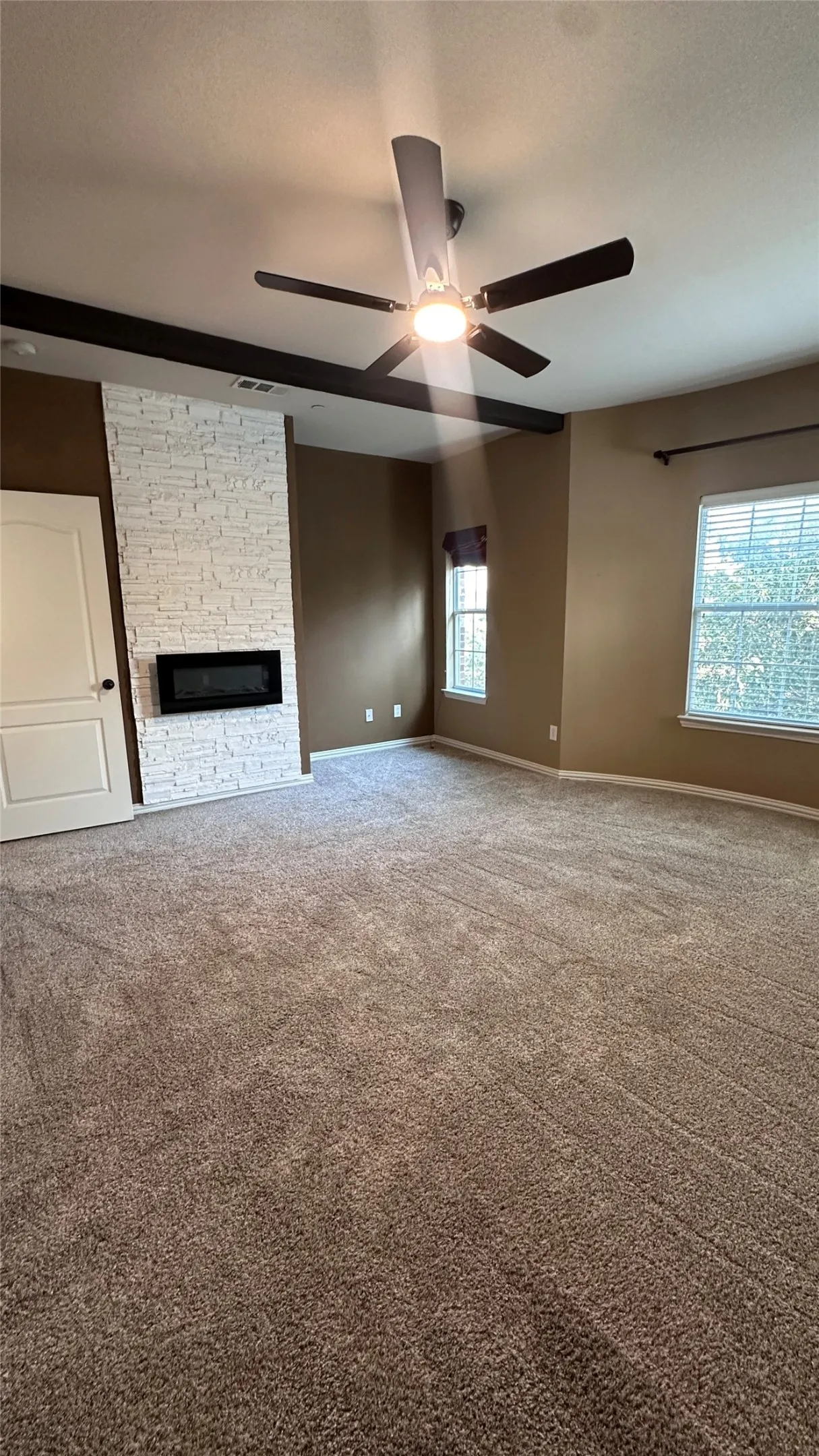 Wall-mounted fireplace with a white stone-finish surround, ceiling fan with integrated lighting, and soft carpet flooring