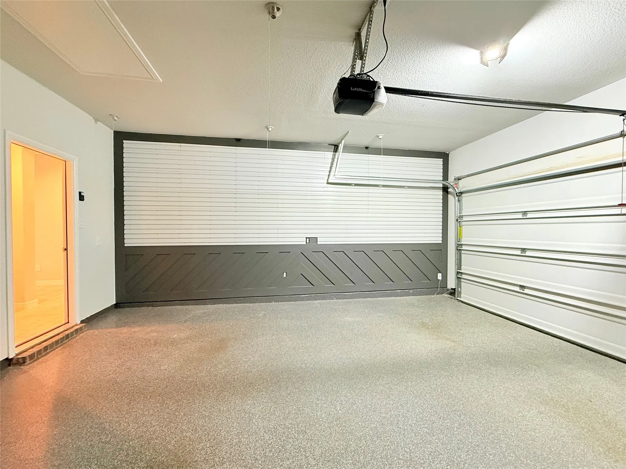 Epoxy-coated concrete flooring, overhead garage door opener, a white garage door, recessed lighting, and a paneled accent wall