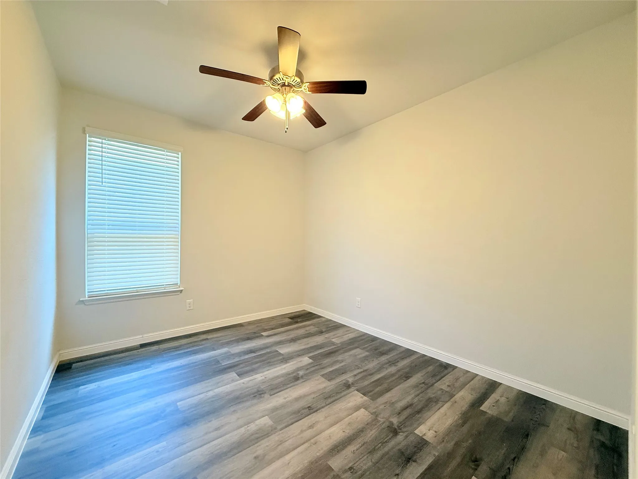 Wood-finish flooring, neutral wall tones, window with horizontal blinds, and a ceiling fan with integrated lighting
