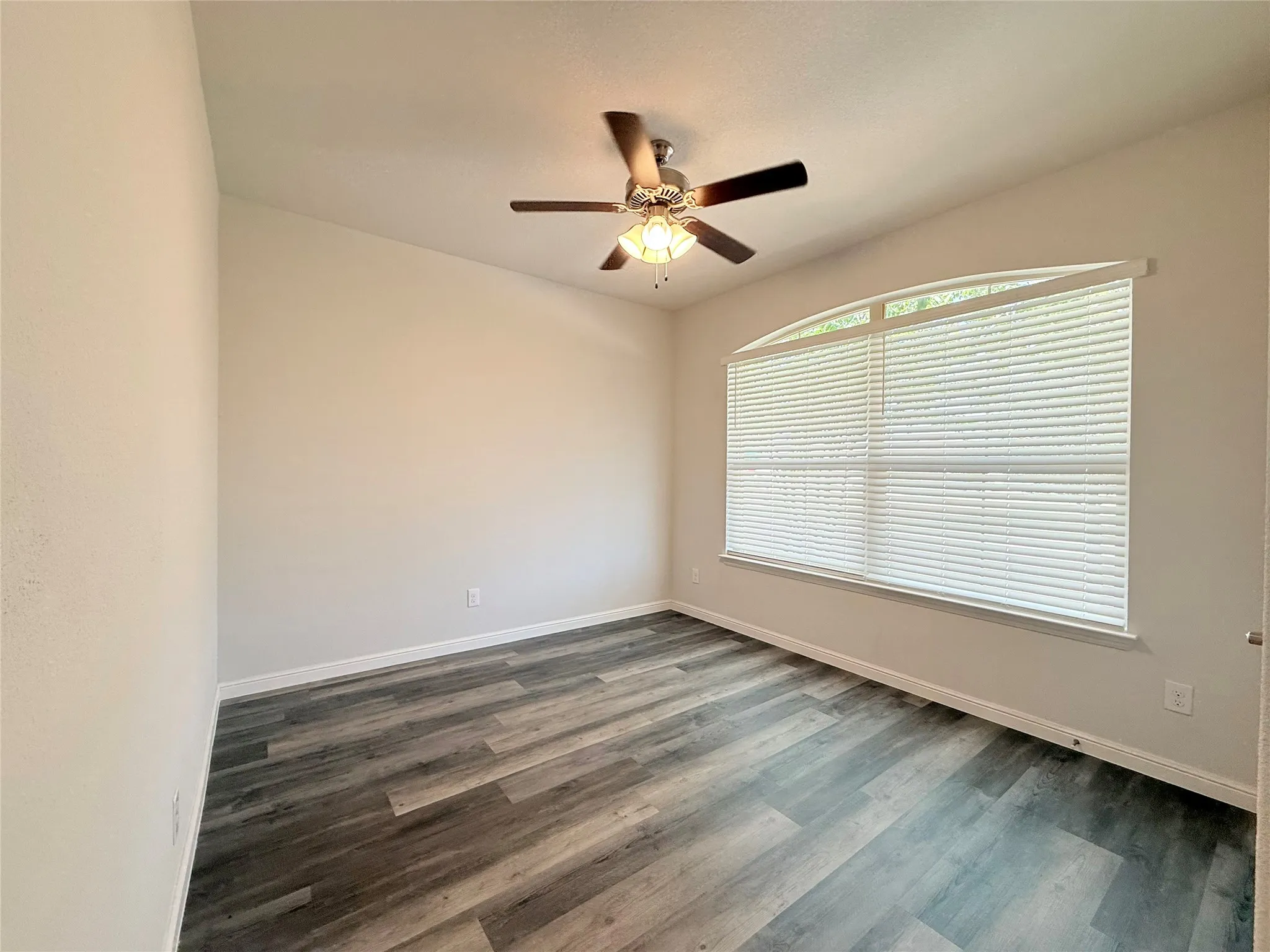 Arched window with blinds, wood-finish flooring, and ceiling fan with integrated lighting