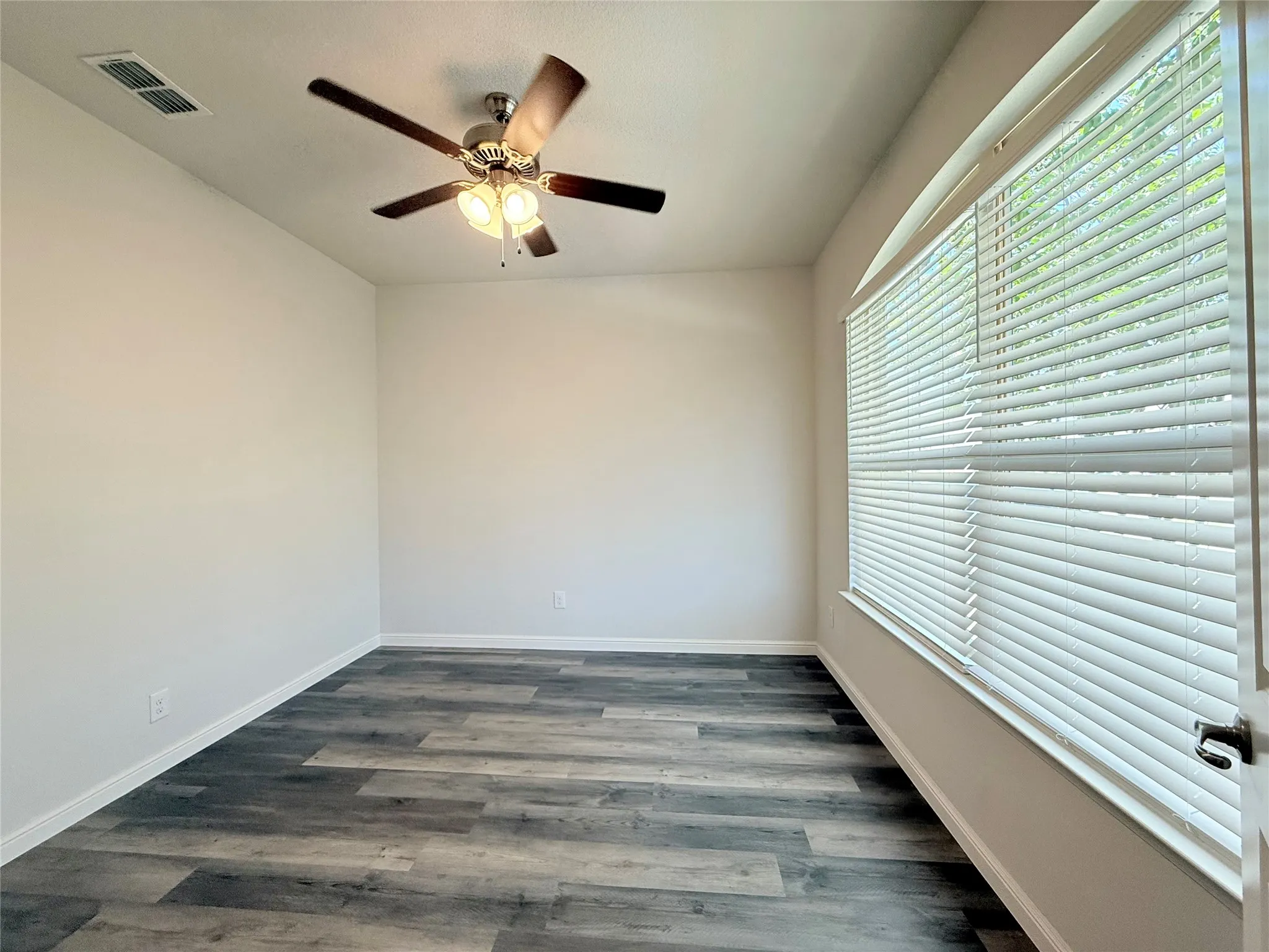 Wood-finish flooring, ceiling fan with integrated lighting, window with blinds, light-toned walls