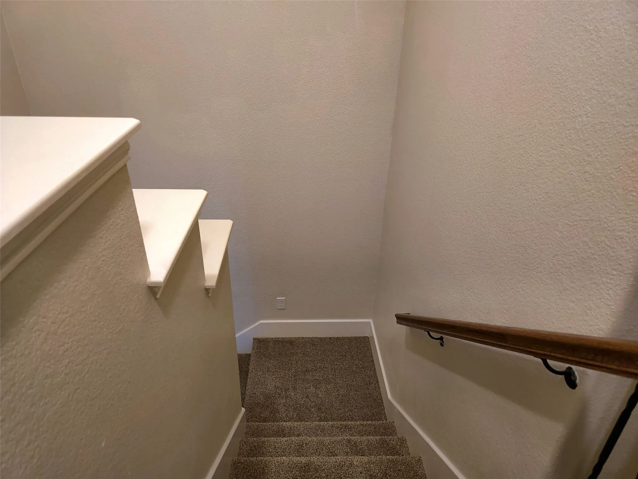 Textured wall finish, white trim, wood-toned handrail, metal handrail brackets, carpeted staircase
